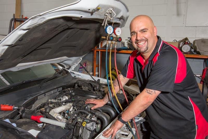 hampstead auto repairs employee smiling for photo with car engine